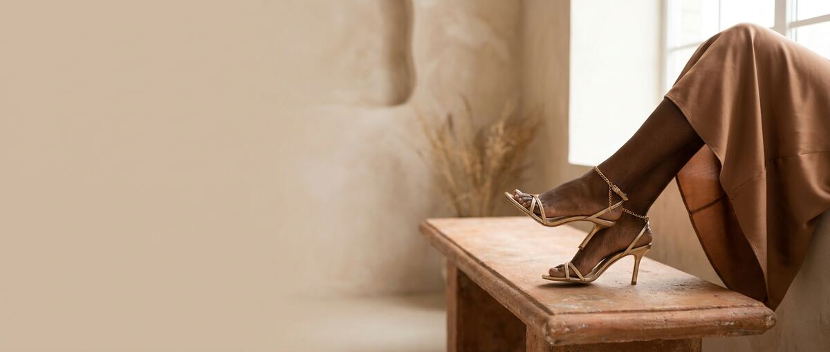 Woman wearing gold strappy heels seated on a wooden bench